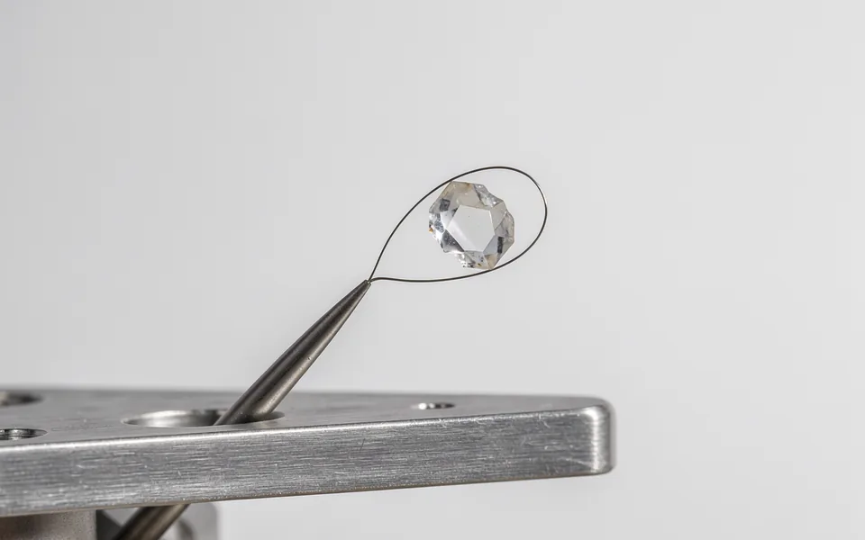 A tiny translucent crystal held in a loop on a metal laboratory mount